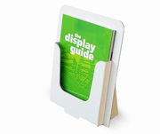 A white cardboad display holder standing on its side, holding a bright green booklet or guide with the words 'the display guide' printed on the cover, against a clean white background.